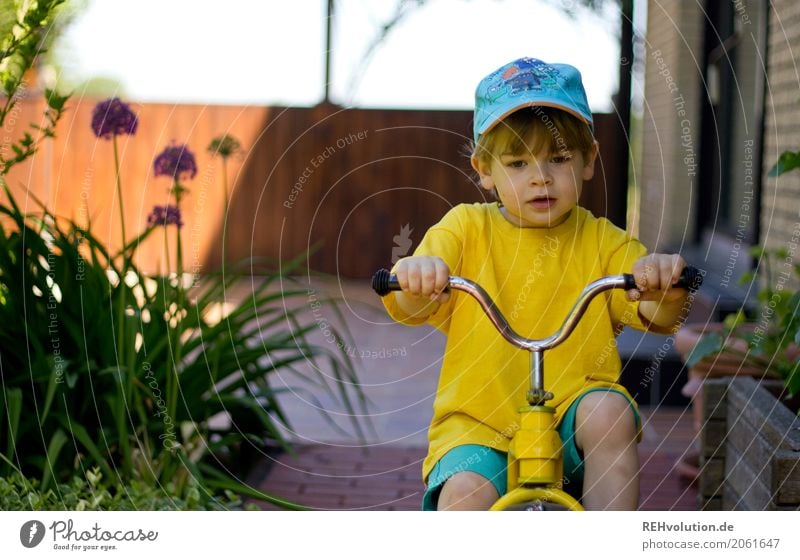 Kind auf einem dreirad Mensch Kleinkind Junge Gesicht 1 1-3 Jahre Natur Sommer Garten authentisch Mütze T-Shirt natürlich Neugier gelb Kindheit Farbfoto