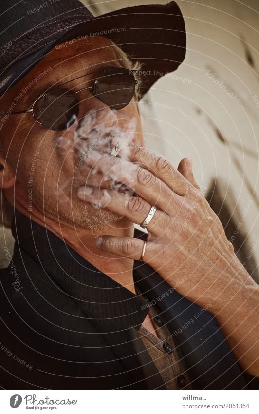 Rauchender Mann mit Schlapphut und dunkler Sonnnenbrille Sonnenbrille Frack weißhaarig Dreitagebart Coolness Bartstoppel Schoßrock Hut Ring lässig rauchend