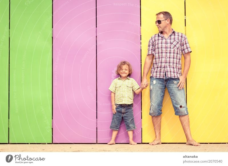 Vater und Sohn entspannen sich in der Nähe des Hauses am Tag. Sie stehen in der Nähe sind die bunten Wand. Konzept der freundlichen Familie. Lifestyle Freude