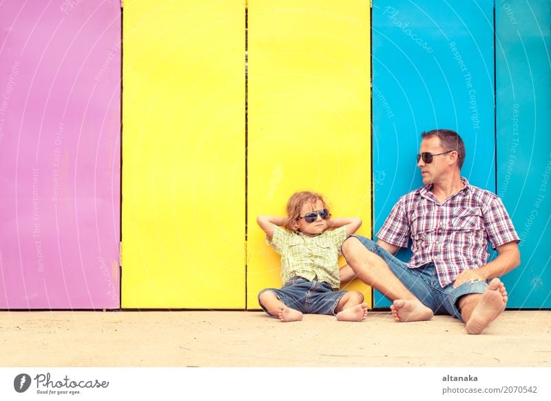 Vater und Sohn entspannen in der Nähe des Hauses in der Tageszeit. Sie sitzen in der Nähe sind die bunten Wand. Konzept der freundlichen Familie. Lifestyle