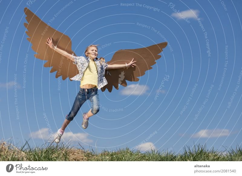 Kleines Mädchen, das tagsüber im Park mit Spielzeugflügeln aus Pappe spielt. Konzept des glücklichen Spiels. Kind hat Spaß im Freien. Bild vor dem Hintergrund des blauen Himmels.