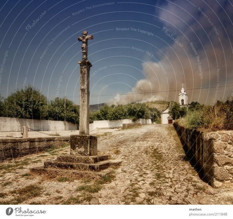 Himmel und Hölle Schönes Wetter Dorf Kirche Platz Mauer Wand Stein blau braun gefährlich Kreuz Kruzifix Rauch Feuer Farbfoto Gedeckte Farben Außenaufnahme