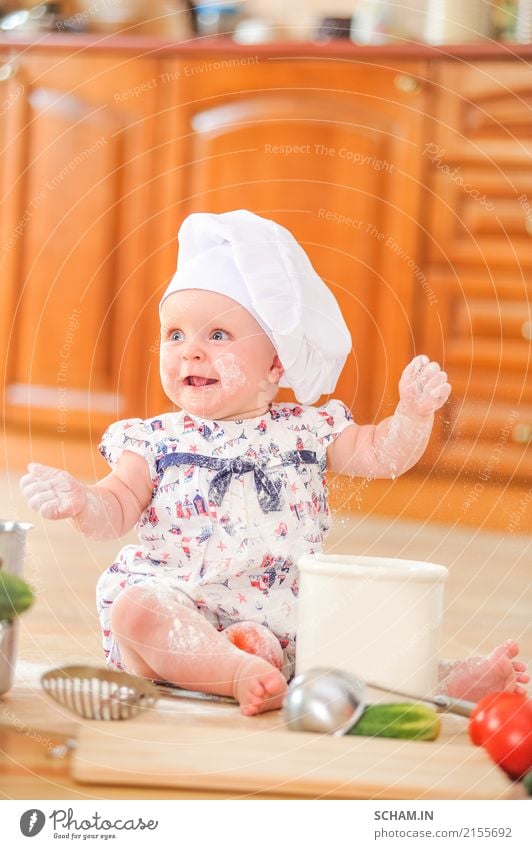 Ein süßes kleines Mädchen mit Kochmütze sitzt auf dem mit Mehl verunreinigten Küchenboden, spielt mit dem Essen, macht Unordnung und hat Spaß Lifestyle Freude