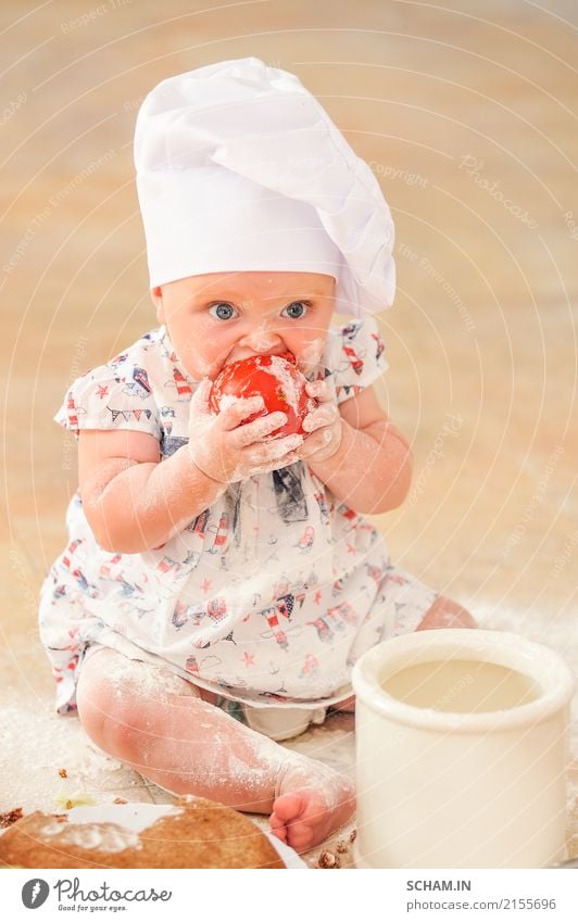 Ein süßes kleines Mädchen mit Kochmütze sitzt auf dem mit Mehl verunreinigten Küchenboden, spielt mit dem Essen, macht Unordnung und hat Spaß Lifestyle Freude