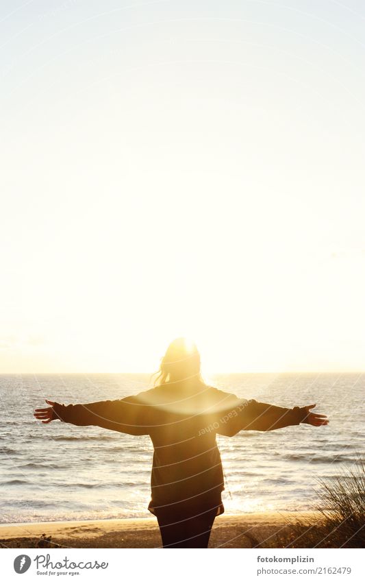 Frau mit ausgestreckten Armen vor leuchtendem Sonnenuntergang am Meer Ferne Freiheit Gleichgewicht Spiritualität Sonnenenergie mental Sonnenaufgang mystisch