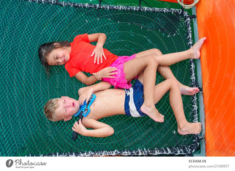 Süße Kinder auf einer Bootsfahrt. Der Junge spielt auf einer Spielzeuggitarre und singt für seine schöne Freundin. Auf der Hängematte des Katamarans liegend, sind die Beine ineinander verschlungen. Blick von oben