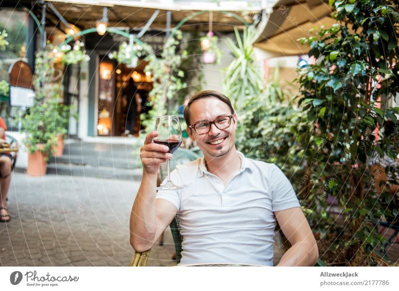 Mann mit Weinglas sitzt im Stuhl und freut sich 1 Mensch Junger Mann sitzen Tag Außenaufnahme Wärme Sommer Rotwein Alkohol trinken Zuprosten Restaurant Terrasse