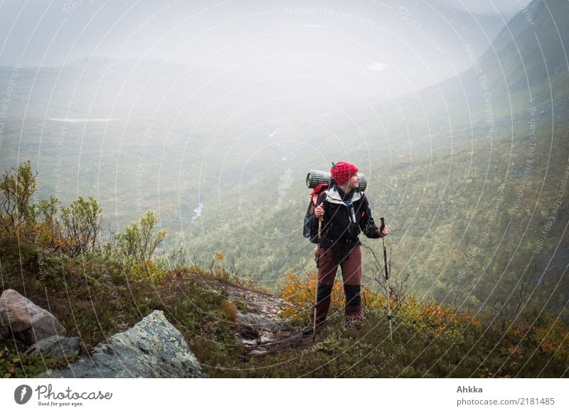 Junge Frau mit Wanderrucksack steht am Rande eines regenverhangenen Tales Entdecker wandern Regen Dunst Nebelschleier Nebelstimmung Herbst Regenwetter Gepäck