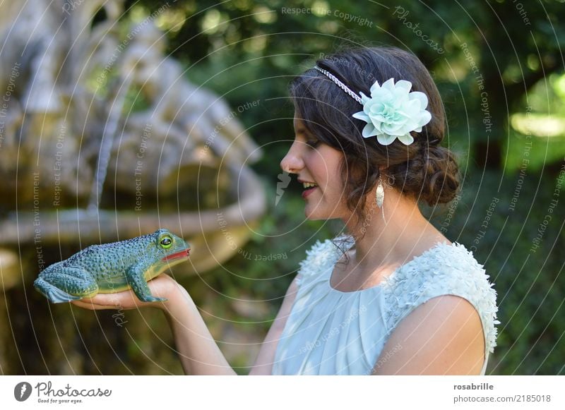 küss mich ....          junge brünette Frau gekleidet wie eine Prinzessin schaut skeptisch einen Frosch auf ihrer Hand an und überlegt, ob sie ihn küssen soll