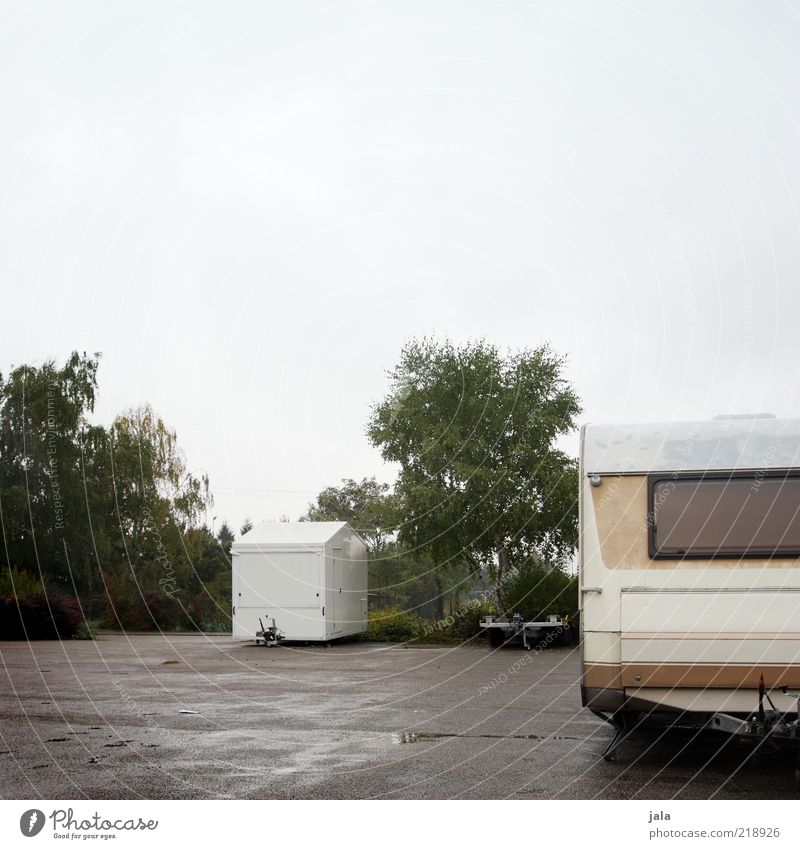 abstellplatz Himmel schlechtes Wetter Pflanze Baum Sträucher Platz Parkplatz Verkehrsmittel Bauwagen Anhänger trist grau grün weiß nass Farbfoto Außenaufnahme