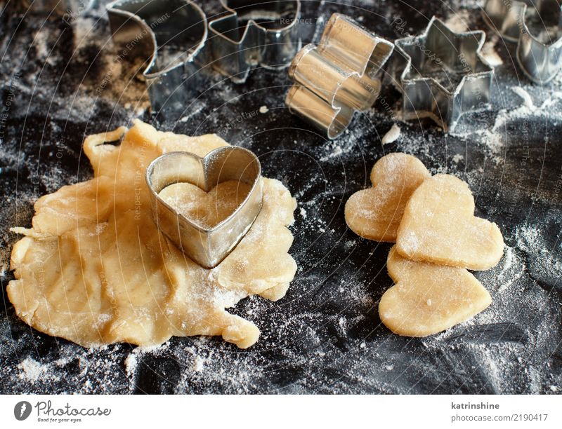 Schließen Sie oben von den Plätzchenschneidern in einem Teig auf einer dunklen Tabelle Teigwaren Backwaren Dessert Küche Herz machen backen Bäckerei Biskuit