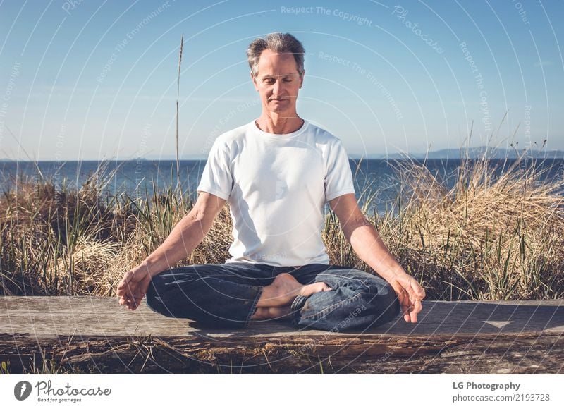 Mann, der in einer entspannten Yogahaltung am Strand sitzt. Erholung Meditation Sonne Erwachsene sitzen natürlich Kraft Gelassenheit 50-60 Jahre Aktion Farbbild