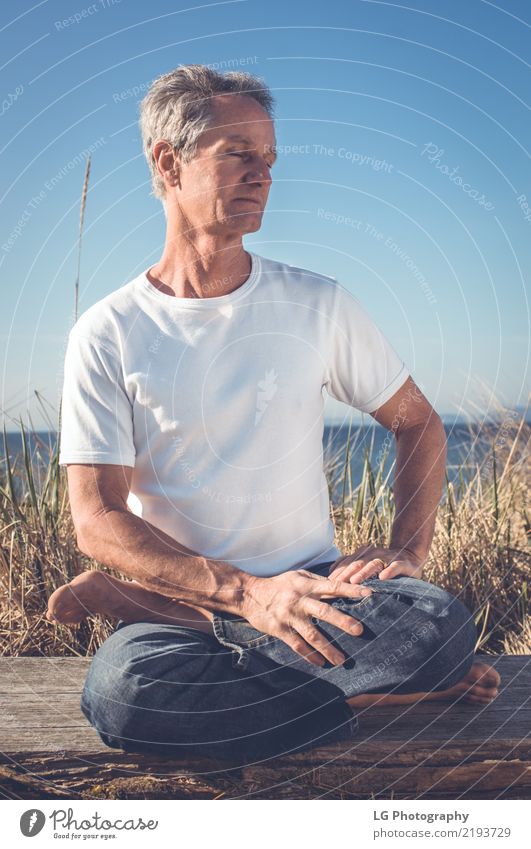 Mann, der in einer entspannten Yogahaltung am Strand sitzt. Erholung Meditation Sonne Erwachsene sitzen natürlich Kraft Gelassenheit 50-60 Jahre Aktion Farbbild