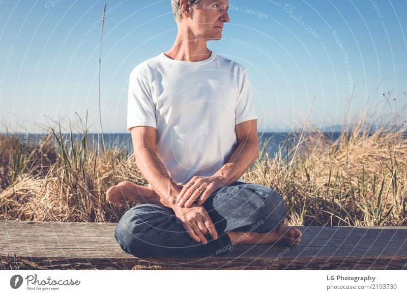 Mann, der in einer entspannten Yogahaltung am Strand sitzt. Erholung Meditation Sonne Erwachsene sitzen natürlich Kraft Gelassenheit 50-60 Jahre Aktion Farbbild