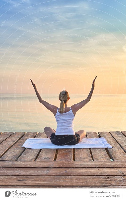 Rear view of young woman sat on towel practicing yoga by sea at sunset looking towards the ocean Wellness Erholung Meditation Ferien & Urlaub & Reisen Sommer