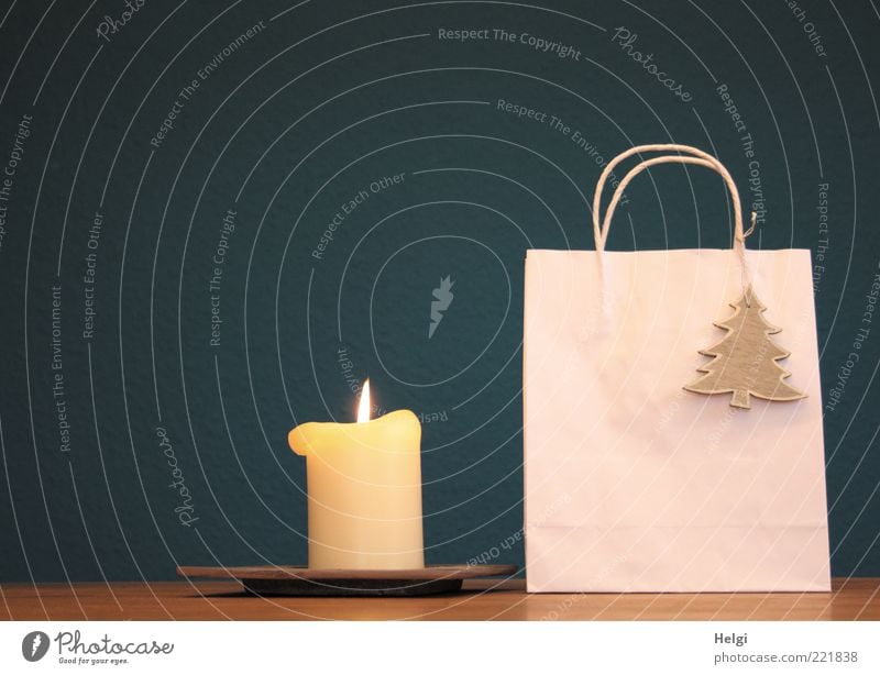 Papiertasche mit Holztannenbaum als Dekoration und brennende Kerze stehen auf einem Tisch vor dunkelblauem Hintergrund Design Dekoration & Verzierung Verpackung