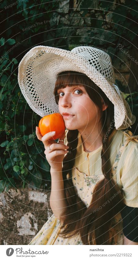 Junge und altmodische Frau, die eine Persimone hält Lebensmittel Gemüse Frucht Orange Ernährung Essen Lifestyle Stil schön Gesundheit Gesunde Ernährung Wellness