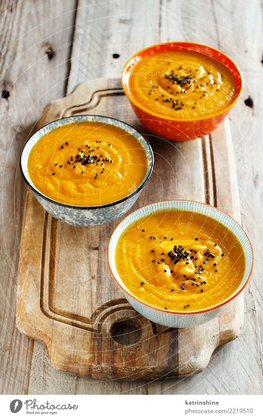 Frische Kürbissuppe in drei Schüsseln auf einem Holztisch Gemüse Suppe Eintopf Vegetarische Ernährung Schalen & Schüsseln Tisch Erntedankfest Halloween Herbst