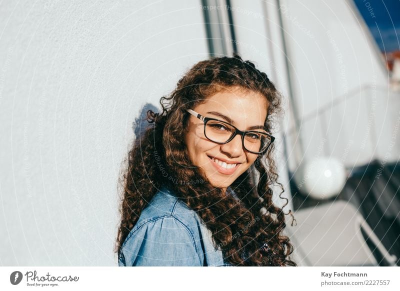 Lächelnde Frau mit lockigem Haar und Brille lehnt an Hauswand Lifestyle Freude Glück schön Haare & Frisuren Wohlgefühl Zufriedenheit feminin Junge Frau