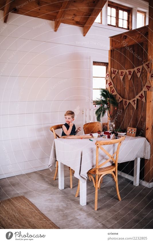 Netter kleiner Junge, der Weihnachtssüßigkeit isst und Geschenke einwickelt Essen Winter Tisch Wohnzimmer Kind Kindheit Hütte sitzen Weihnachten Süßigkeiten