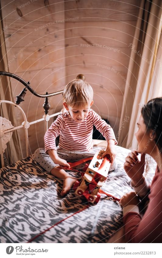 Llittle-Junge, der auf Bettöffnungs-Weihnachtsgeschenken mit Mutter sitzt Freude Glück Winter Haus Kinderzimmer Schlafzimmer Weihnachten & Advent Mensch