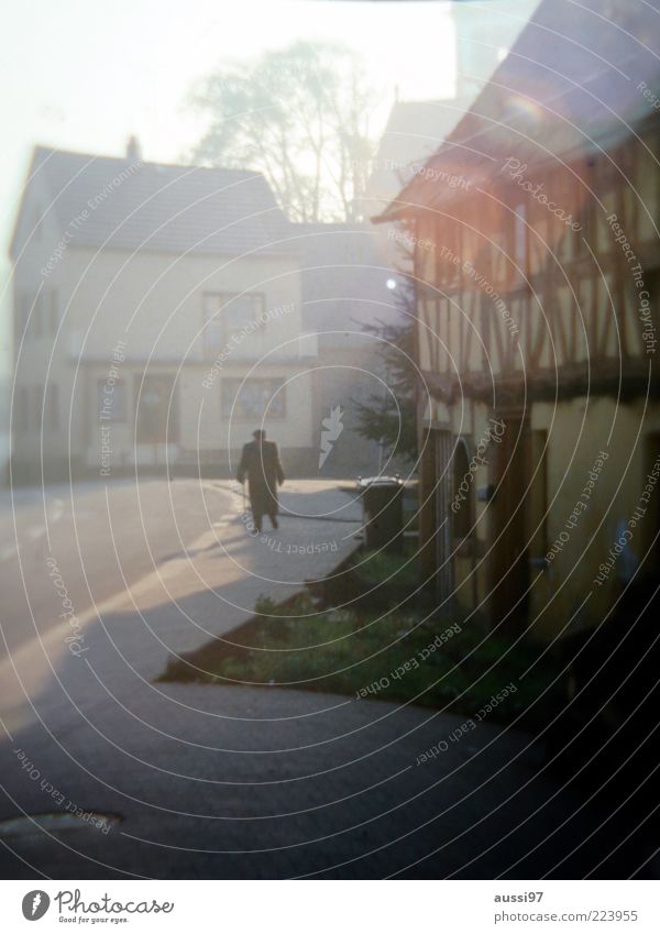 Uncle Albert Mann alt Senior Einsamkeit Ruhestand Spaziergang Unschärfe Sonnenstrahlen Asphalt Teer Fachwerkhaus Dorf Fassade Textfreiraum unten