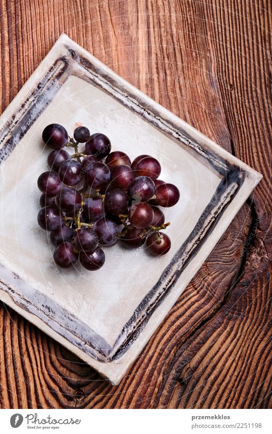 Schwarze Trauben auf handgemachter quadratischer Tonwarenplatte Lebensmittel Frucht Diät Teller Tisch Holz Rost frisch lecker oben Keramik Essen zubereiten