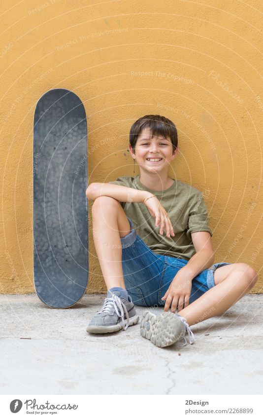 Ein lächelnder Junge mit Skateboard sitzt allein auf dem Boden Lifestyle Freude Erholung Freiheit Sommer Sonne Kind Funktelefon PDA Mensch Mann Erwachsene