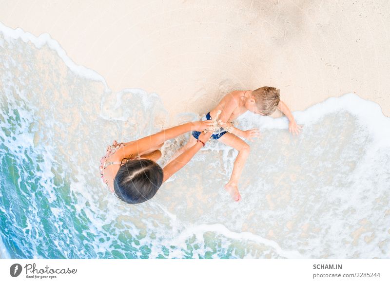 Ein süßer Junge und ein süßes Mädchen haben Spaß am sonnigen tropischen Strand. Auf Sand liegend, wunderbare Wellen um sie herum. Blick von oben Lifestyle