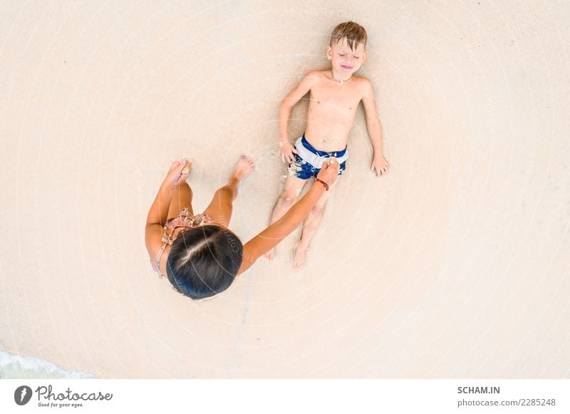 Ein süßer Junge und ein süßes Mädchen haben Spaß am sonnigen tropischen Strand. Auf Sand liegend, wunderbare Wellen um sie herum. Blick von oben Lifestyle