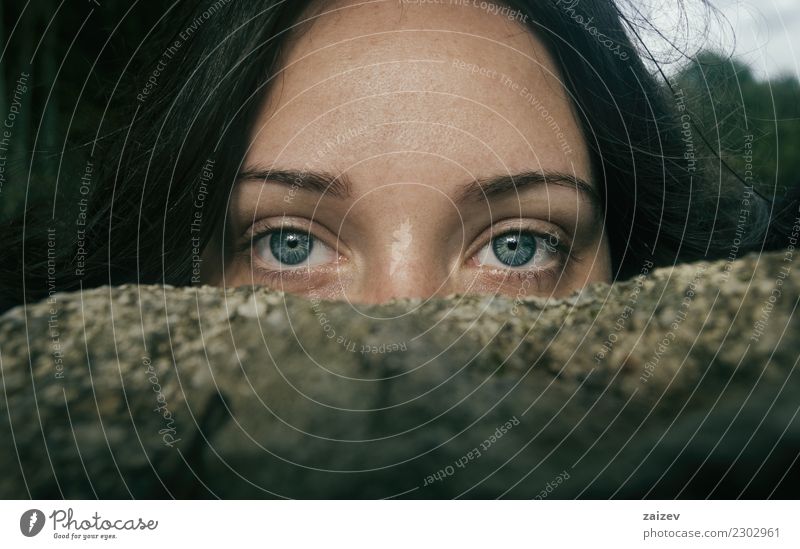 Chica de ojos azules y grandes mirando a camara por encima de una piedra tapandose la mitad de la cara Fotokamera Frau Erwachsene Stein Denken entdecken