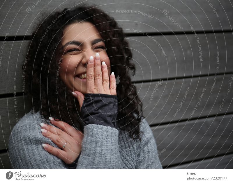 Nikolija feminin Frau Erwachsene 1 Mensch Mauer Wand Pullover brünett langhaarig Locken Holz festhalten lachen Freundlichkeit Fröhlichkeit Glück Stimmung Freude