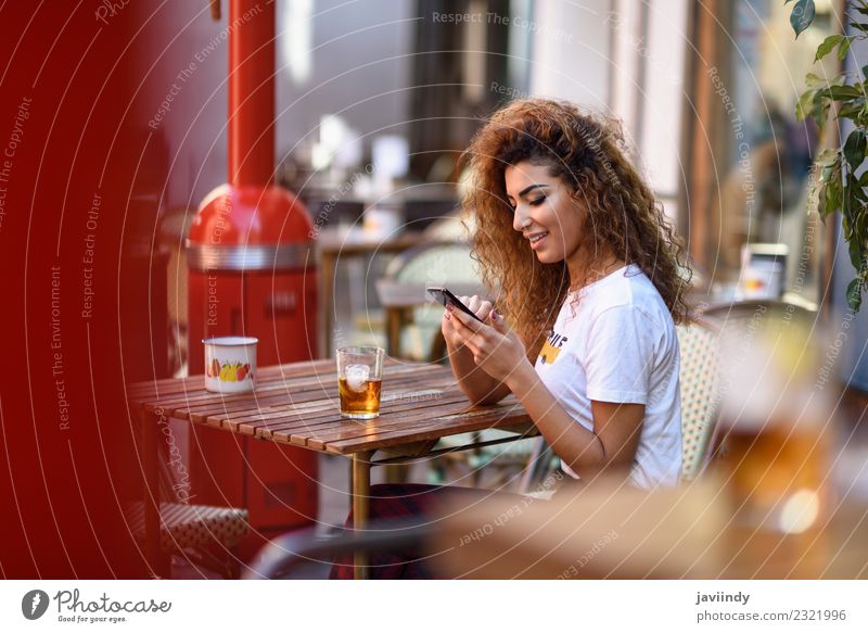 Mädchen, das in einer Straßenbar sitzt und auf ihr Smartphone schaut. Getränk Lifestyle Stil Glück schön Haare & Frisuren Freizeit & Hobby Restaurant Telefon