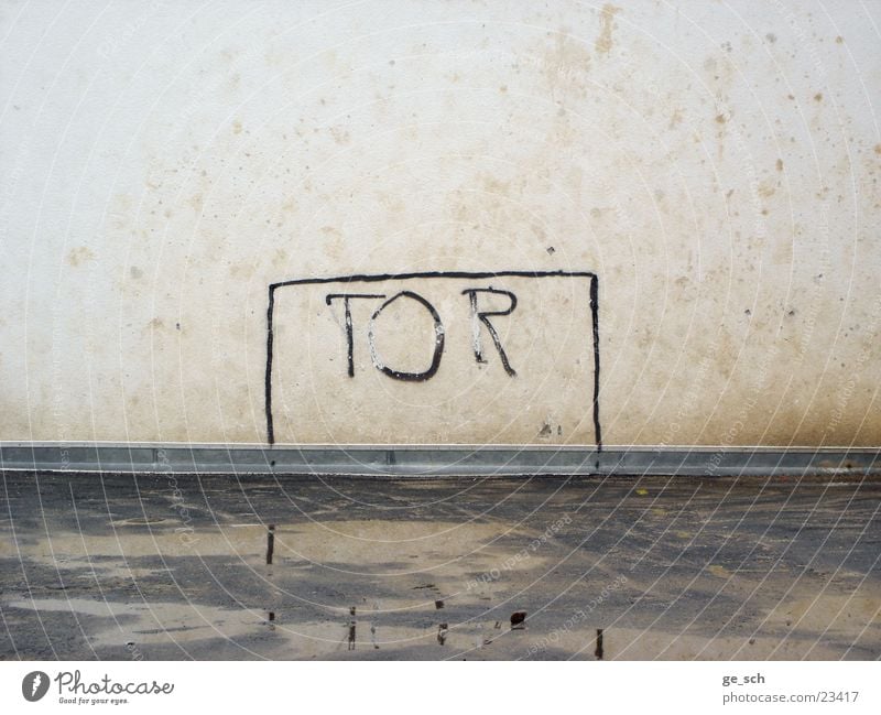 Tooor Spielplatz Hinterhof Wand Linie Buchstaben Spielfeld Sport Fußballplatz schäbig Tor Pfütze Menschenleer trist Wasserspiegelung Farbfoto Außenaufnahme