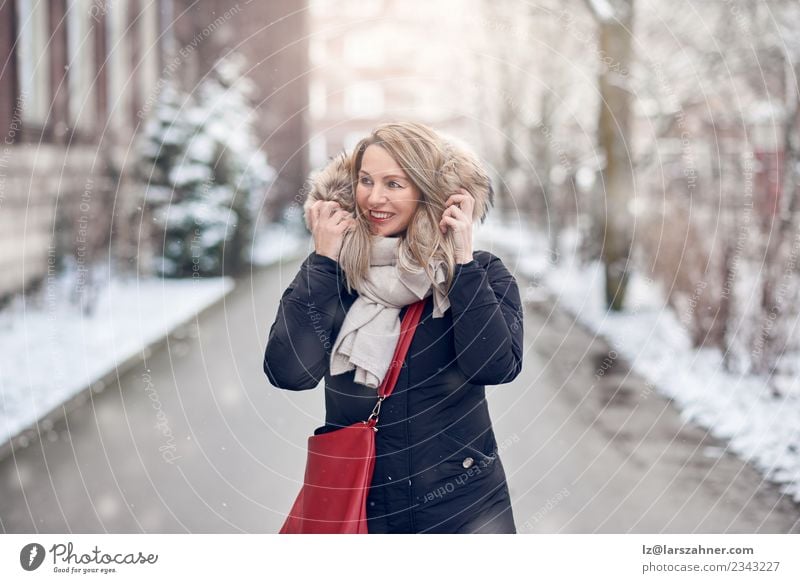 Lächelnde junge Frau, die auf einer verschneiten Straße geht. Glück schön Winter Schnee Erwachsene 1 Mensch 45-60 Jahre Natur Wetter Mode Jacke Mantel