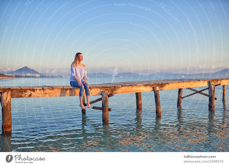 Barfuß-Frau, die bei Sonnenuntergang auf einem Küstenpier sitzt. Lifestyle Glück schön Freizeit & Hobby Ferien & Urlaub & Reisen Freiheit Sommer Strand Meer