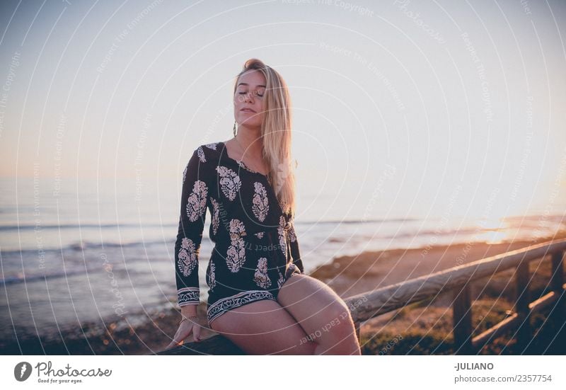 Junges Mädchen sitzt und genießt den Blick auf den Sonnenuntergang am Meer. Strand blond Coolness Abenddämmerung Freude Güte lachen Lifestyle retro Sand Lächeln