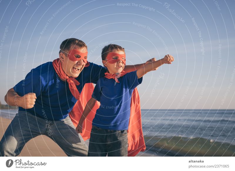 Vater und Sohn spielen tagsüber am Strand Superhelden. Die Leute haben Spaß im Freien. Konzept des Sommerurlaubs und der freundlichen Familie. Lifestyle Freude