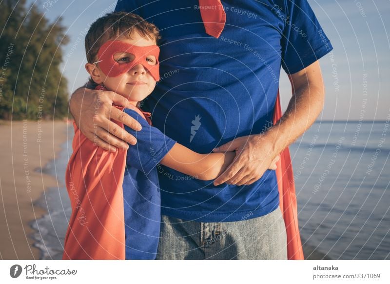 Vater und Sohn spielen tagsüber am Strand Superhelden. Die Leute haben Spaß im Freien. Konzept des Sommerurlaubs und der freundlichen Familie. Lifestyle Freude