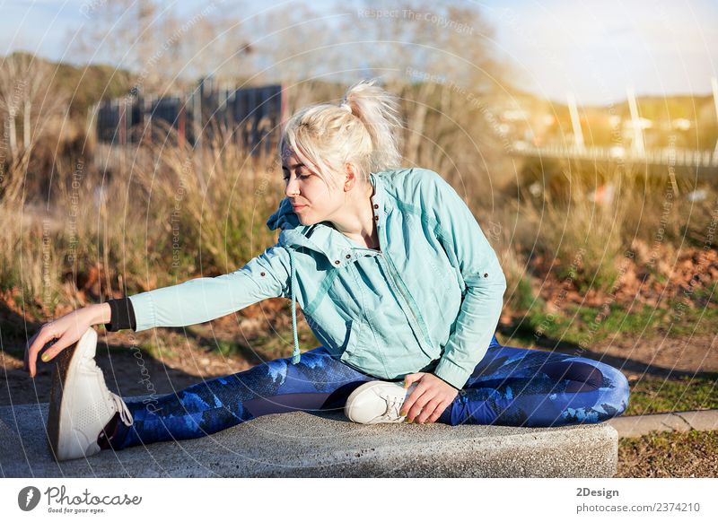 blonde Frau, die im Gras sitzt und sich in einem Park ausstreckt. Lifestyle Glück schön Körper Freizeit & Hobby Sport Leichtathletik Sportler Joggen Mensch