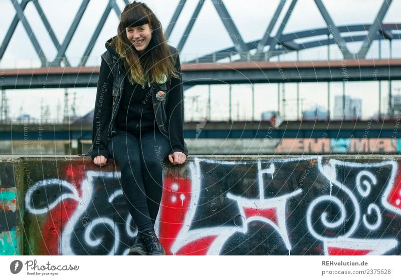 Junge Frau sitzt auf einer Mauer Blick in die Kamera Ganzkörperaufnahme Porträt Schwache Tiefenschärfe Unschärfe Tag Außenaufnahme Farbfoto rebellisch natürlich