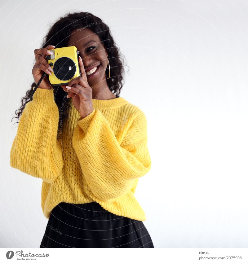 Apolline feminin Frau Erwachsene 1 Mensch Rock Pullover Ohrringe schwarzhaarig langhaarig Locken Fotokamera beobachten Lächeln lachen Blick stehen schön gelb