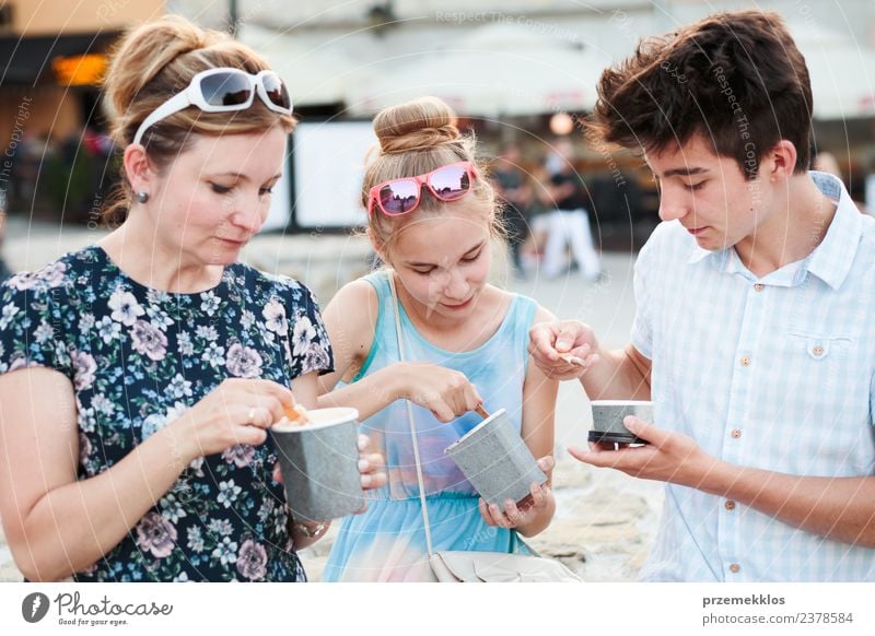 Familien, die im Stadtzentrum Zeit miteinander verbringen, genießen es, an einem Sommertag Eiscreme zu essen. Mutter, Teenager, Mädchen und Junge verbringen an sonnigen Nachmittagen viel Zeit miteinander und essen ein süßes Dessert. Stadtzentrum, Altstadt im Hintergrund