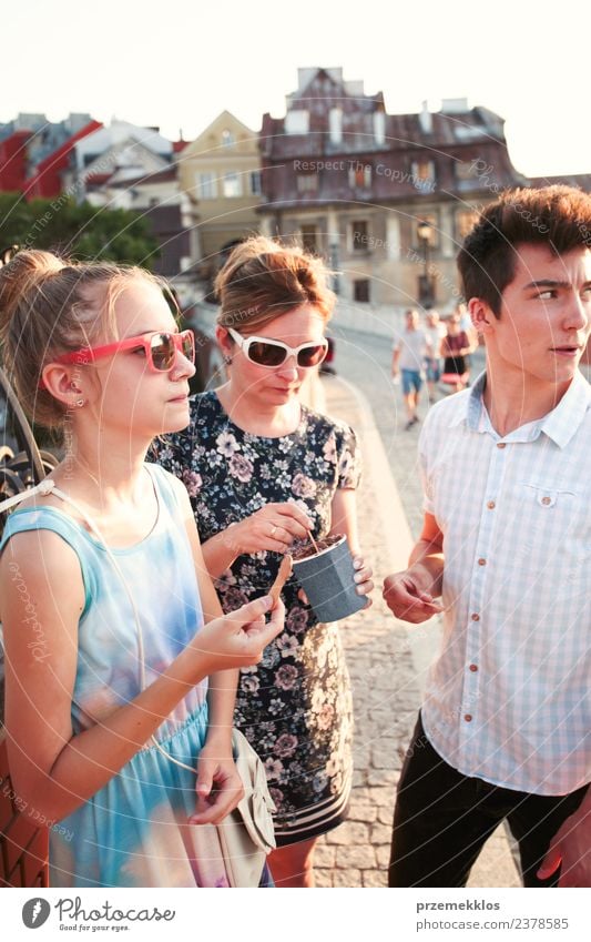 Familien, die im Stadtzentrum Zeit miteinander verbringen, genießen es, an einem Sommertag Eiscreme zu essen. Mutter, Teenager, Mädchen und Junge verbringen an sonnigen Nachmittagen viel Zeit miteinander und essen ein süßes Dessert. Stadtzentrum, Altstadt im Hintergrund