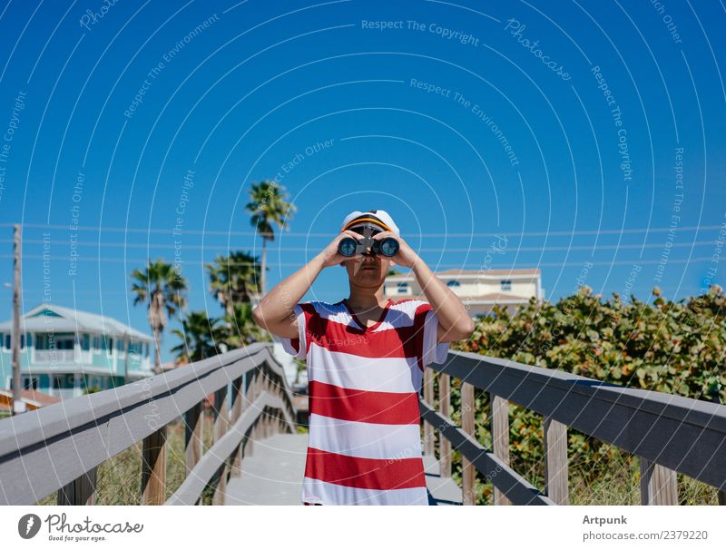 Ein junger Seemann, der durch ein Fernglas schaut. Matrosen Sommer Strand Ferien & Urlaub & Reisen Hut Kapitän Palme tropisch Anlegestelle Pflanze Sand Baum