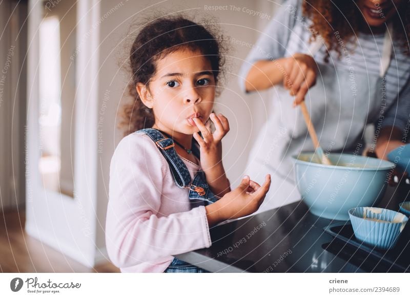 Das kleine afrikanische Mädchen leckt den Teig von den Fingern. Dessert Freude Glück schön Küche Kind Mensch Frau Erwachsene Mutter Kindheit Zusammensein lecker