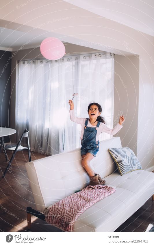 Afrikanisches glückliches Mädchen spielt mit einem Ballon auf der Couch. Freude Glück schön Spielen Wohnzimmer Kind Kindheit Luftballon Lächeln Fröhlichkeit