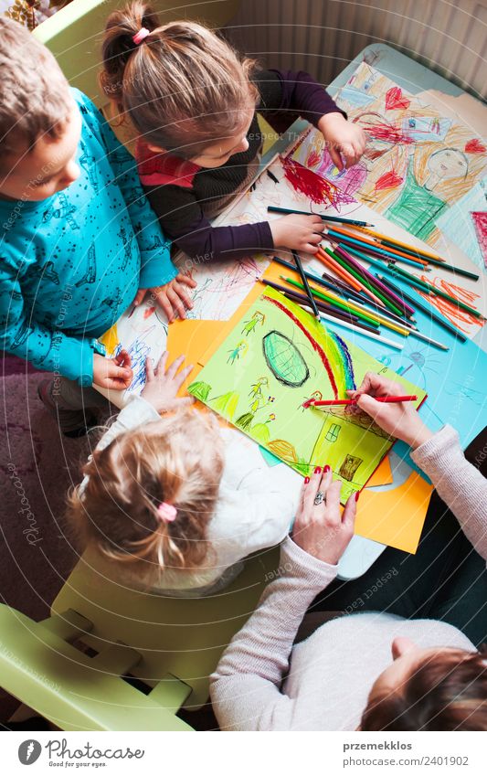 Mutter mit ihren kleinen Töchtern und ihrem Sohn, die am Tisch sitzend ein buntes Bild von spielenden Kindern mit Buntstiften zeichnen. Foto von oben Lifestyle