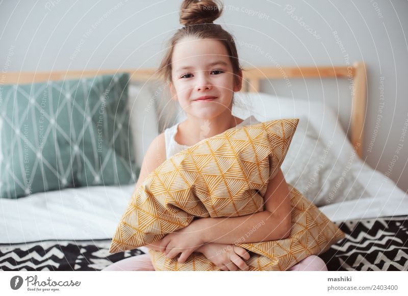 fröhliches Kind Mädchen sitzt auf dem Bett und umarmt Kissen Lifestyle Freude Erholung Schlafzimmer Lächeln schlafen träumen klein lustig niedlich bequem