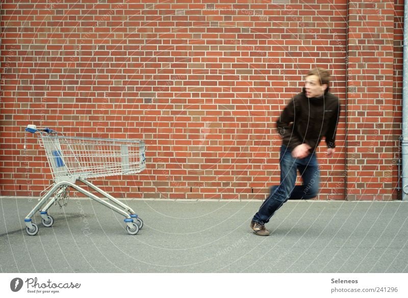 Shoppingtour Wirtschaft Handel Mensch maskulin Mann Erwachsene 1 Haus Mauer Wand Straße Jeanshose Jacke Einkaufswagen Backstein laufen stehen Geschwindigkeit